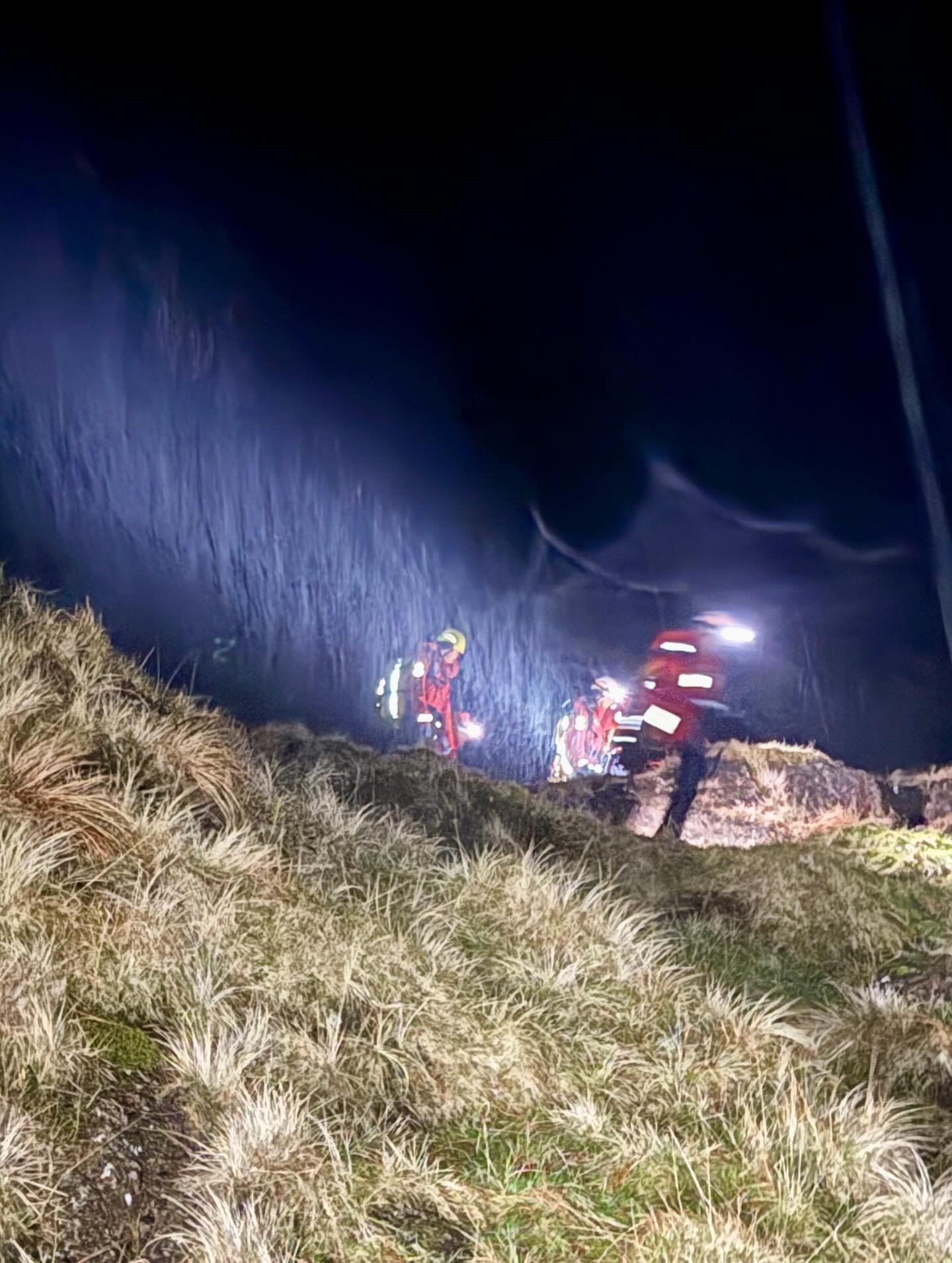 Head torches picking out mountain rescue team members on a dark crag at night.