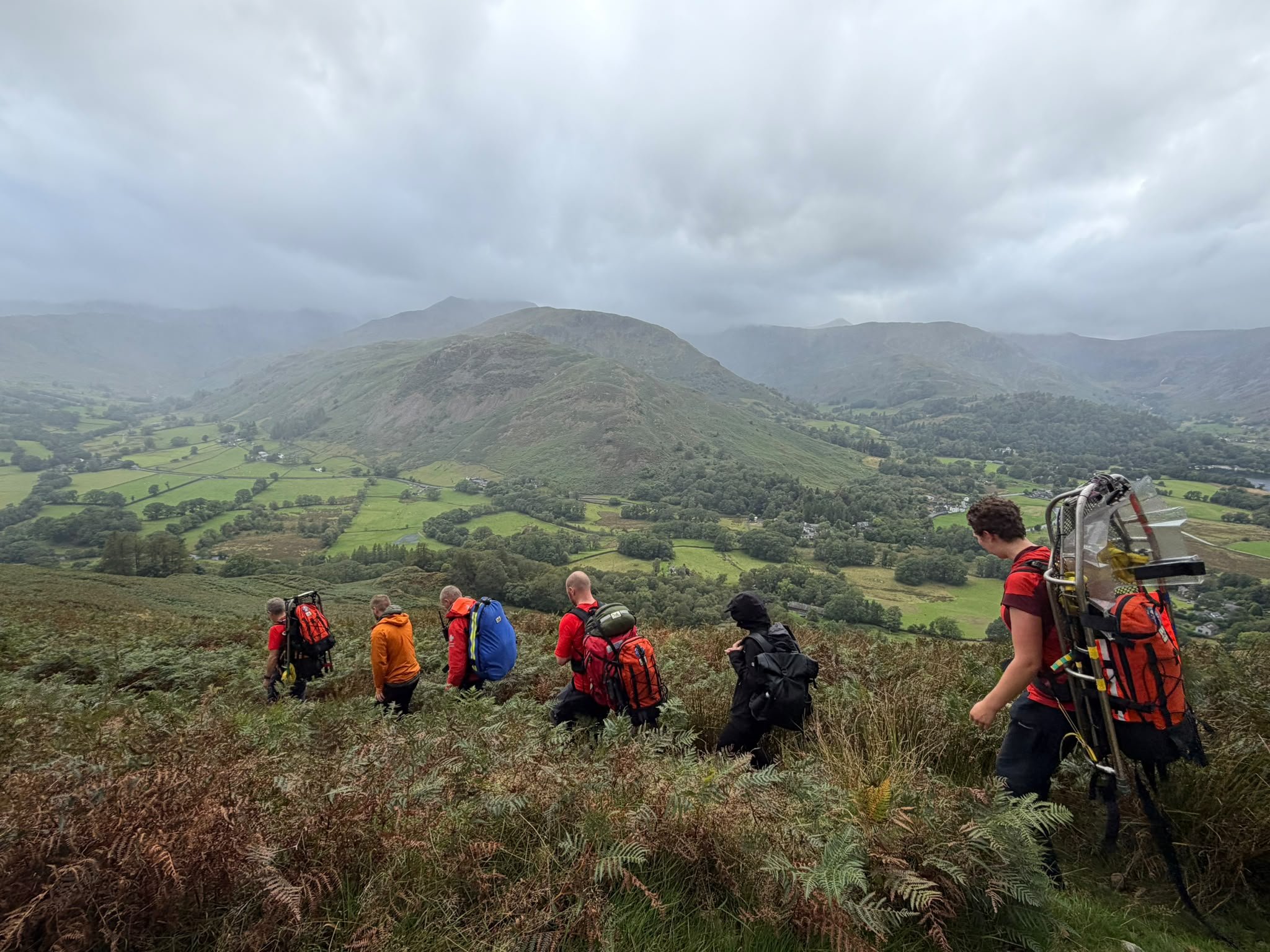Team members in red kit descending the bracken slopes above Patterdale, with the valley below