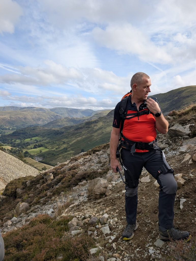 A team member with a radio on the rocky slope above the valley