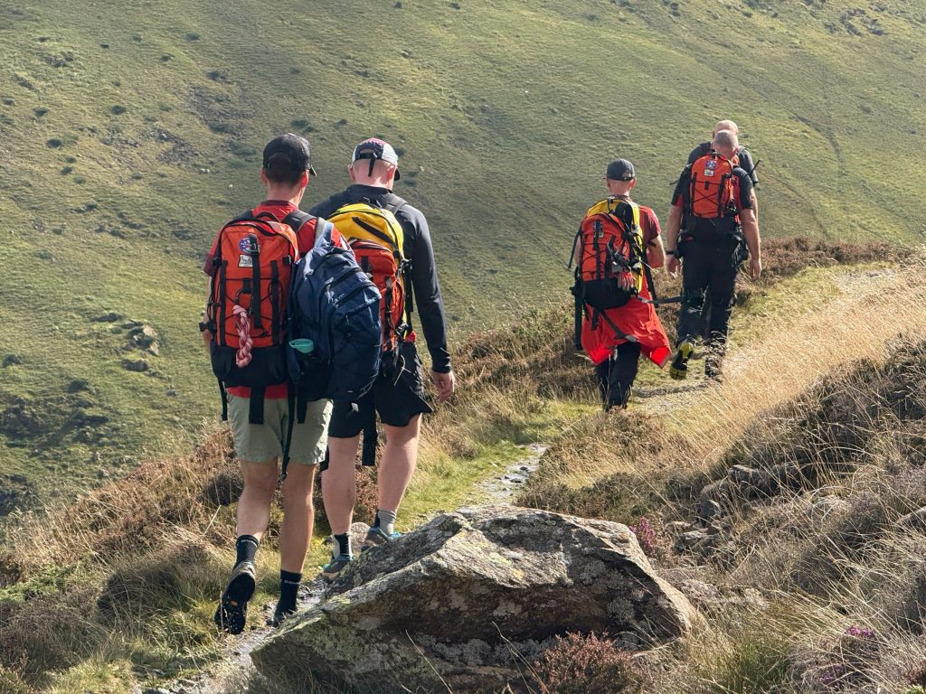Team members with rucksacks walking along a fellside path