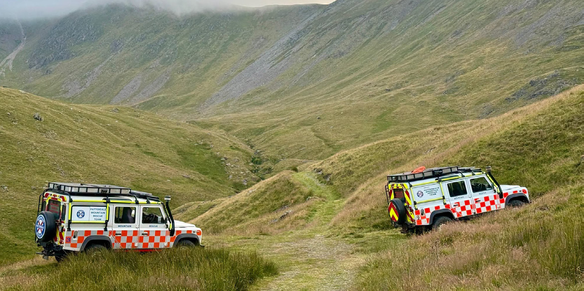 Two team Land Rovers on a grassy track in a fell valley
