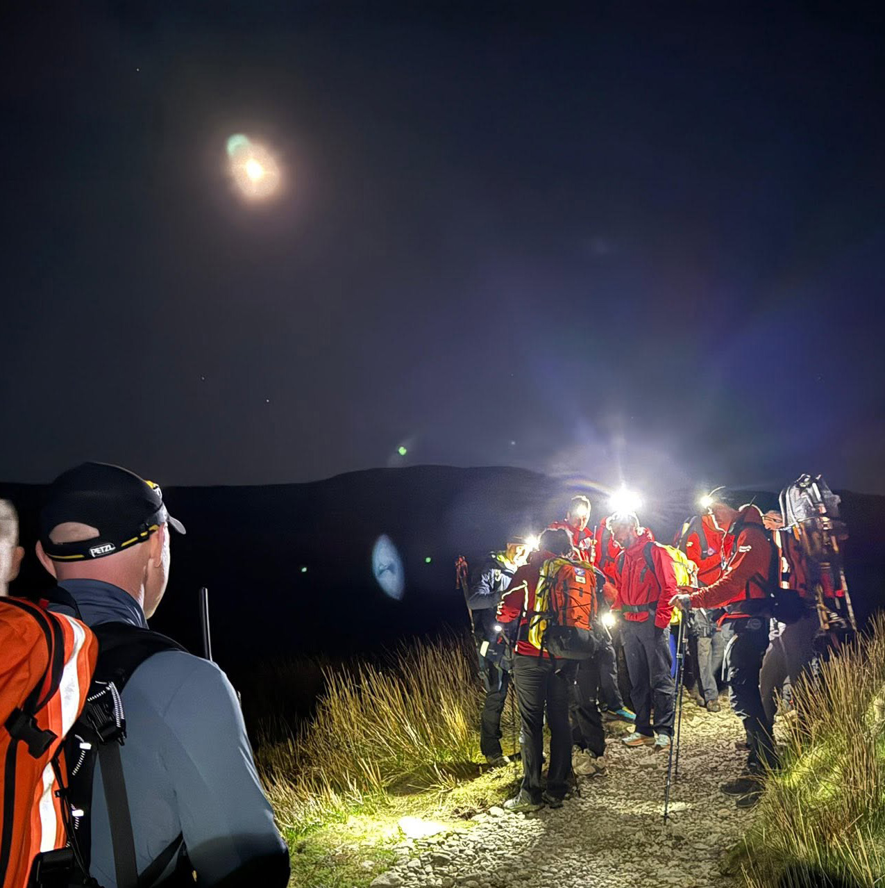 Team members with head torches gathered on a fell path at night during a callout